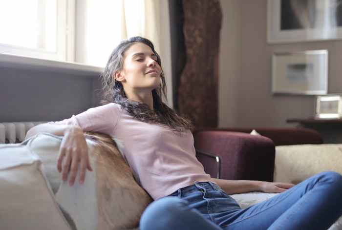 photo of woman in pink long sleeve shirt and blue denim jeans sitting on brown sofa with her eyes closed